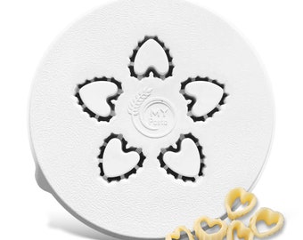 May include: A white pasta maker with heart-shaped cutouts and the text "MY Pasta." Several heart-shaped pasta pieces are scattered below. The pasta maker has a textured surface.