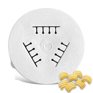 May include: White plastic pasta maker attachment with a design of three rows of holes. The attachment is designed to make a type of pasta that looks like small, curved shells. There are several of these pasta shells in the lower right corner of the image.