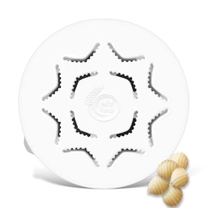 May include: A white pasta maker with a star-shaped design, featuring multiple cut-out sections. The centre has a wheat emblem and the text "MY Pasta". Several pieces of pasta are visible on the right side.