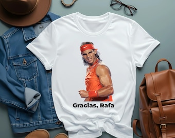 May include: White t-shirt with a photo of a tennis player wearing a red headband and orange tank top. The text "Gracias, Rafa" is printed on the shirt.