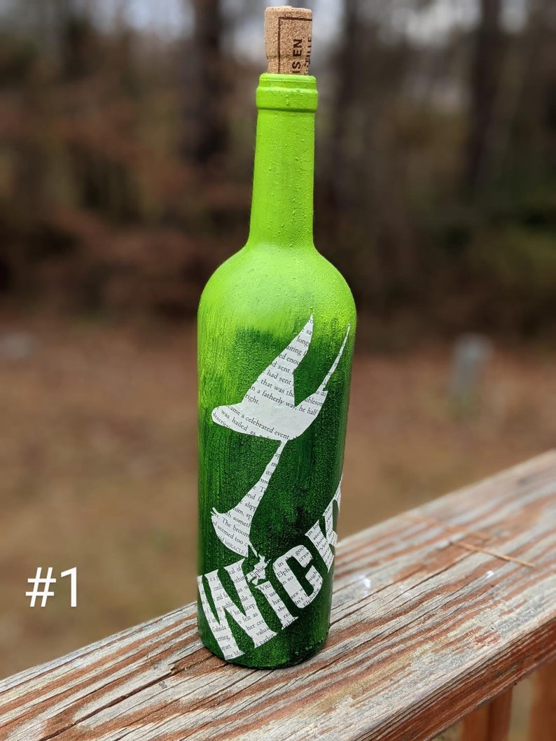 Puede incluir: Una botella de vidrio verde con un tap&oacute;n de corcho. La botella est&aacute; decorada con una silueta blanca de un p&aacute;jaro y la palabra "Wick" en letras blancas. La botella est&aacute; sobre una superficie de madera.
