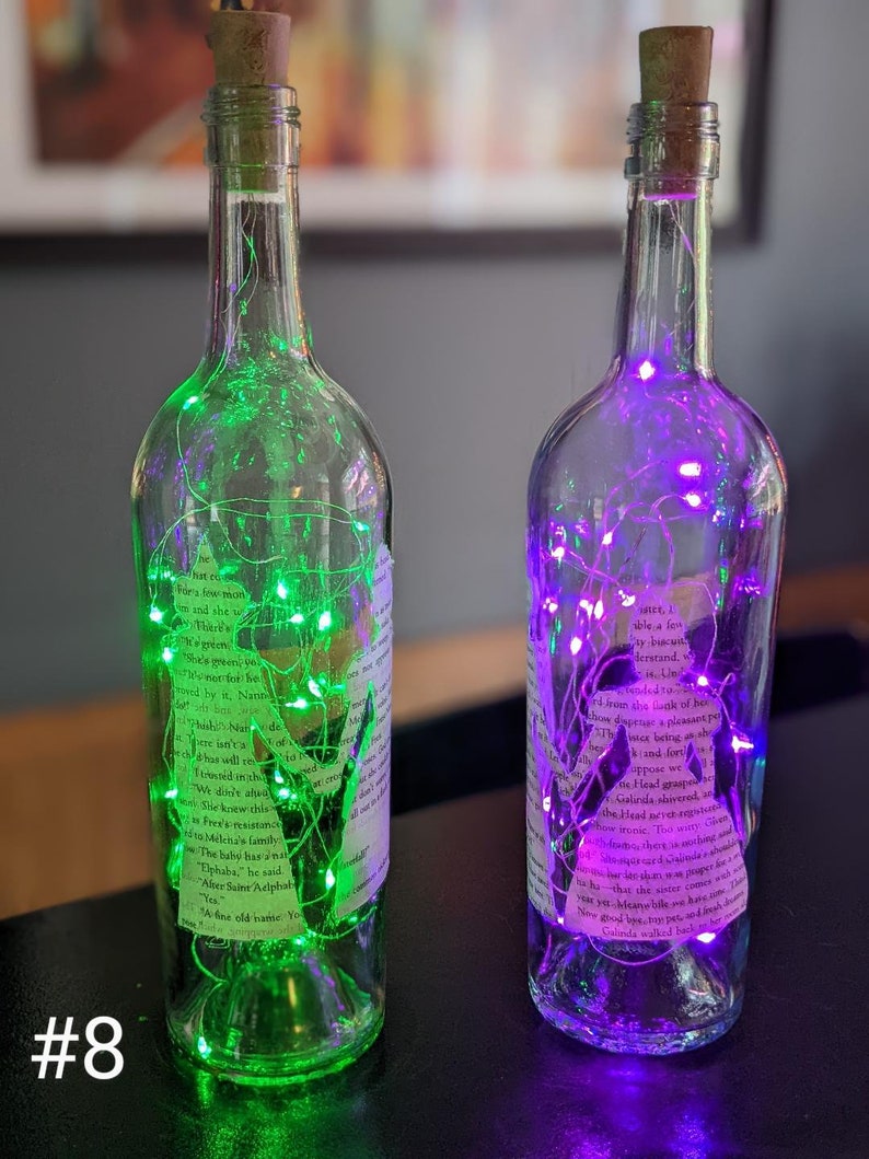 Puede incluir: Dos botellas de vidrio con tapas de corcho, llenas de luces de hadas coloridas. Las botellas est&aacute;n decoradas con etiquetas de papel impresas y tienen un aspecto vintage.