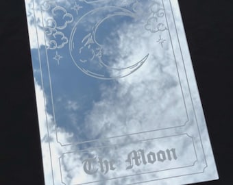 May include: A rectangular mirror featuring an etched design of a crescent moon with a face, surrounded by clouds and stars. The Roman numeral XVIII is etched at the top, and the text The Moon is etched at the bottom in a gothic-style font.