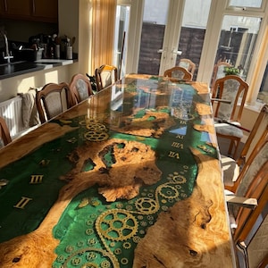 May include: A large wooden dining table with a green epoxy resin top. The resin has gold-colored gears and Roman numerals embedded in it. The table is surrounded by wooden chairs.