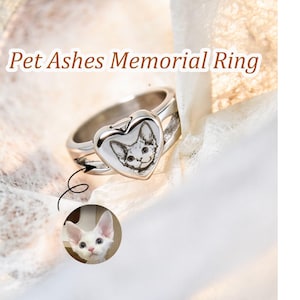 May include: A silver-toned metal ring featuring a heart-shaped face with an engraved portrait of a cat. The text Pet Ashes Memorial Ring is displayed above the ring, and a small circular inset shows the original photograph of the white cat.