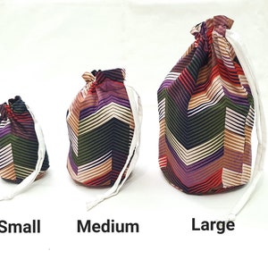 May include: Three drawstring bags in different sizes, small, medium, and large. The bags are made of fabric with a colorful geometric pattern of stripes and zigzags in shades of purple, red, brown, green, and white.