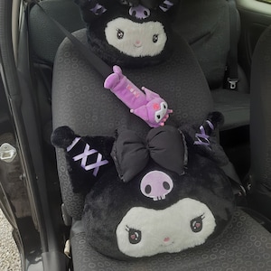 Könnte beinhalten: Schwarz-weißes Plüschtier mit Totenkopf und Schleife. Das Spielzeug befindet sich in einem Autositz mit einem lila und schwarzen Sicherheitsgurt.