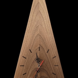 Op de afbeelding: Een driehoekige houten klok met een natuurlijke houtnerf afwerking. De klok heeft zwarte uurmarkeringen en sierlijke zwarte wijzers met een rode secondewijzer. De wijzerplaat is lichtbruin van kleur. De merknaam "HolzWeltSlezak" staat onderaan.