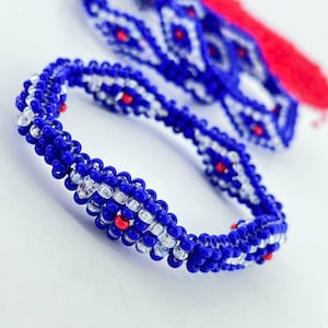 May include: A close-up of a blue and white beaded bracelet with red accents. The bracelet is made of small, round beads and has a simple, elegant design.