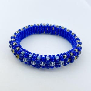 May include: A circular beaded bracelet constructed from vibrant royal blue seed beads. The design features a repeating pattern of faceted clear crystal beads interspersed with smaller metallic silver beads, creating a textured, multi-layered appearance.