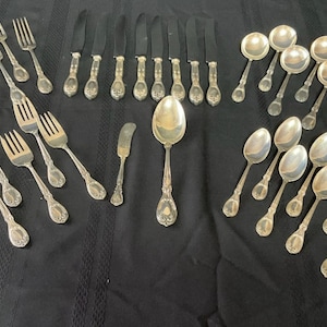 May include: A set of silver cutlery, including forks, knives, and spoons. The set includes a variety of sizes and styles of spoons, including soup spoons and teaspoons.