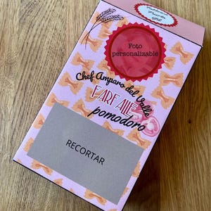 May include: A rectangular cardboard pasta box with a light pink background featuring a repeating pattern of orange farfalle pasta. The box displays the text Chef Amparo del Valle, FARFALLE pomodoro, Fabbrica Puerta Gil, Foto personalizable, and RECORTAR.