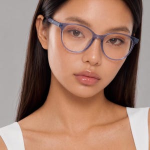 May include: A pair of eyeglasses featuring translucent, light purple, rounded frames. The glasses have a smooth, polished finish with thin temples and a bridge that connects the two circular lenses. The design is simple, focusing on the frame shape.