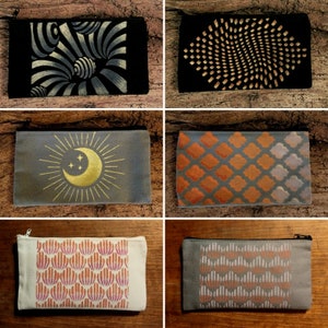 May include: Six different zippered pouches with various patterns. The pouches are made of a canvas material and have a black zipper. The patterns include a gold crescent moon and sun, a gold geometric pattern, a gold and black swirl pattern, a grey and orange geometric pattern, a white and orange geometric pattern, and a grey and orange geometric pattern.
