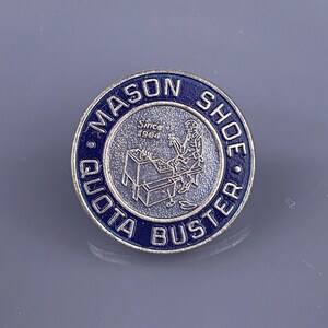 May include: A blue and silver pin with the text "Mason Shoe Quota Buster" and "Since 1964" around a depiction of a shoe repairman working at a bench.