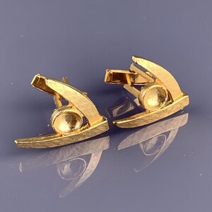 May include: A pair of gold cufflinks with a textured finish. Each cufflink features a curved design with a round center.