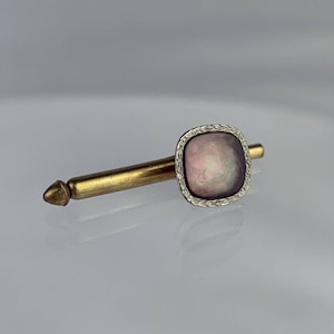 May include: A gold tie tack with a square-shaped iridescent abalone shell set in a silver frame.