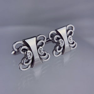 May include: A pair of silver cufflinks with a decorative butterfly design.