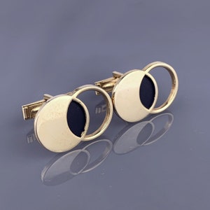 May include: A pair of gold cufflinks with black enamel accents. Each cufflink features two interlocking circles, one larger than the other.