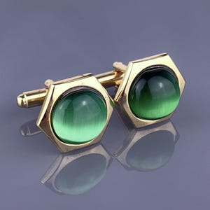 May include: A pair of gold cufflinks with green glass cabochons. The cufflinks are hexagonal in shape.