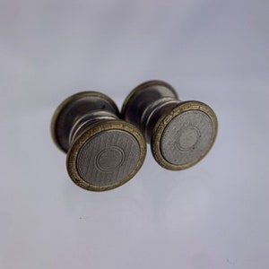 May include: A pair of silver cufflinks with a gold-coloured trim and a circular design. The cufflinks have a textured surface.