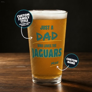 May include: A clear glass pint filled with golden beer, featuring teal text that reads JUST A DAD WHO LOVES THE JAGUARS and the name MIKE. Two circular callout labels indicate areas for a custom family title and a custom name personalization.