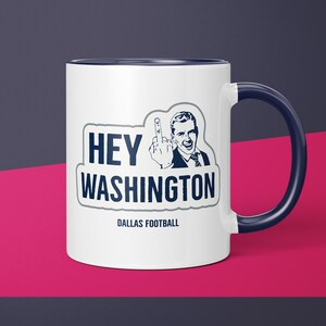 May include: White ceramic mug with a navy blue interior and handle. The mug features the text "HEY WASHINGTON" in navy blue, along with an illustration of a man giving the middle finger. The words "DALLAS FOOTBALL" are printed below.