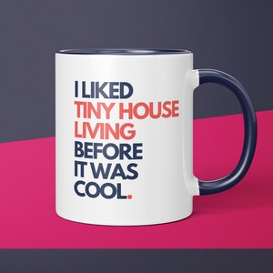 May include: White ceramic coffee mug with a blue rim and handle. The mug has text that reads "I LIKED TINY HOUSE LIVING BEFORE IT WAS COOL."