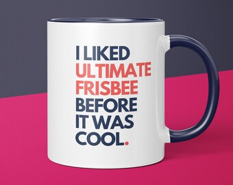 May include: White ceramic coffee mug with a blue rim and handle. The mug has the text "I LIKED ULTIMATE FRISBEE BEFORE IT WAS COOL." printed in blue and red.