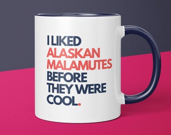 May include: White ceramic coffee mug with a blue rim and handle. The mug has black text that reads "I LIKED ALASKAN MALAMUTES BEFORE THEY WERE COOL."