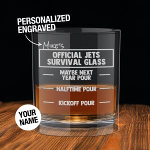 May include: A personalized engraved glass with the text "Mike's Official Jets Survival Glass." The glass has fill lines labeled "Maybe Next Year Pour," "Halftime Pour," and "Kickoff Pour." The words "Your Name" are also visible.