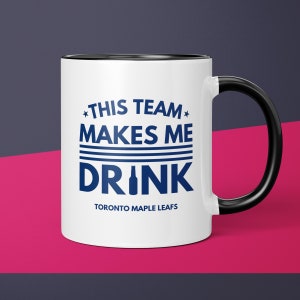 May include: White ceramic coffee mug with a black rim and handle. The mug has a blue graphic that says "*THIS TEAM* MAKES ME DRINK TORONTO MAPLE LEAFS".