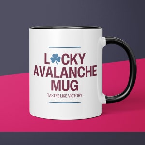 May include: White ceramic mug with a black rim and handle. The mug has a blue shamrock and the text "Lucky Avalanche Mug" in maroon and blue. The text "Tastes like victory" is printed in maroon below the main text.