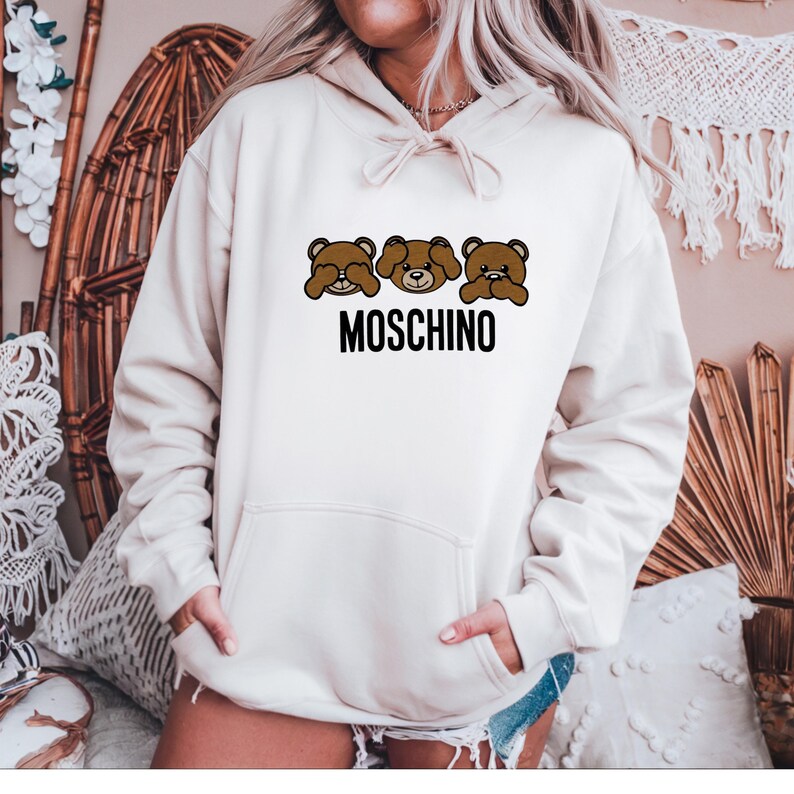 May include: White hoodie with a brown bear graphic and the text "MOSCHINO" printed on the front.