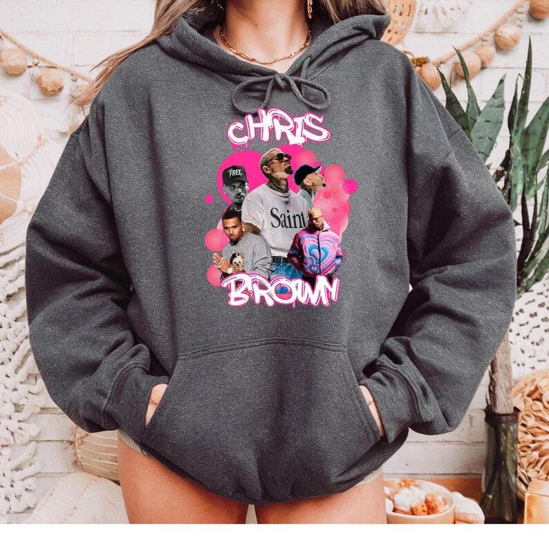 May include: A dark gray hoodie with a pink graphic print of Chris Brown. The graphic features multiple images of Chris Brown in different poses and outfits. The text "Chris Brown" is written in pink letters above the images.