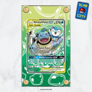 May include: A framed Pokémon trading card featuring Blastoise and Piplup. The card has a green and yellow design with the text "Blastoise & Piplup GX 270 HP TAG TEAM". The frame is green with bubble accents and gold-colored fasteners. A "SLAB CITY" sticker is in the upper right corner.