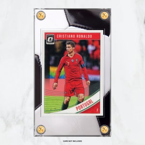 May include: A clear plastic slab with a black and white background. Inside the slab is a trading card featuring Cristiano Ronaldo in a red and green soccer uniform. The card has the Optic logo and the text "Cristiano Ronaldo" and "Portugal".