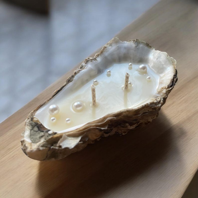 Close-up of an oyster shell candle with two wicks and pearls. The candle is illuminated by soft light and rests on a smooth wooden surface.