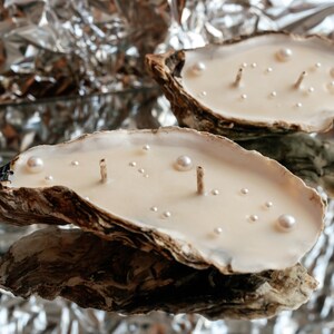 Two oyster shell candles with pearl decorations on a shiny silver foil background.