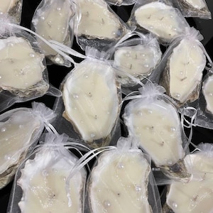Multiple double-wick oyster shell candles with pearls, each carefully packaged in a semi-transparent white organza bag with drawstrings.