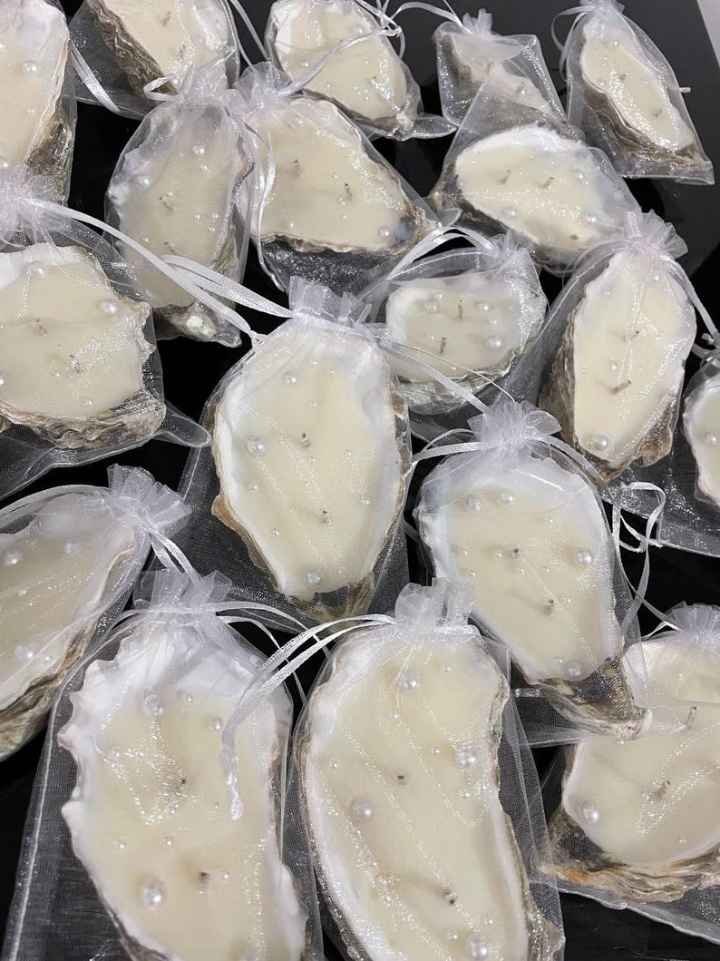 Multiple double-wick oyster shell candles with pearls, each carefully packaged in a semi-transparent white organza bag with drawstrings.