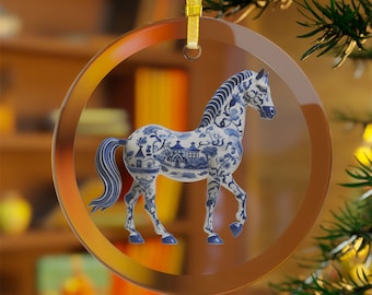 May include: A round glass ornament with a blue and white porcelain horse design. The horse is depicted in a walking pose with a flowing tail and mane. The ornament has a gold ribbon attached to the top.