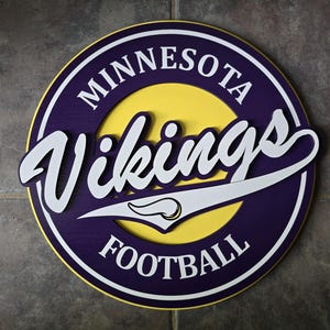 May include: A round wooden sign featuring the Minnesota Vikings logo. The sign has a purple outer ring with the words "MINNESOTA" and "FOOTBALL" in white. The center is yellow, with the word "Vikings" in white script.