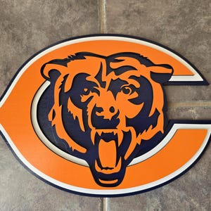 May include: A wooden Chicago Bears logo with a navy blue bear head and orange and white background.