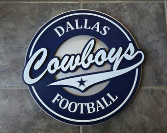 May include: A blue and white wooden sign with the words "Dallas Cowboys Football" in a white circle on a blue background.