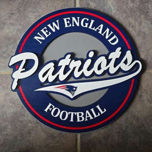 May include: A blue and red circular sign with the words "New England Patriots Football" in white lettering. The Patriots logo is in the center of the sign.