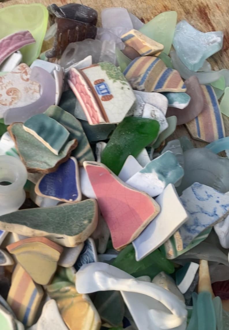 May include: A collection of sea glass and pottery shards in various colors. Pieces include green, blue, pink, and white fragments, some with striped or patterned designs. The image showcases a variety of shapes and textures, suggesting a beachcombing theme.