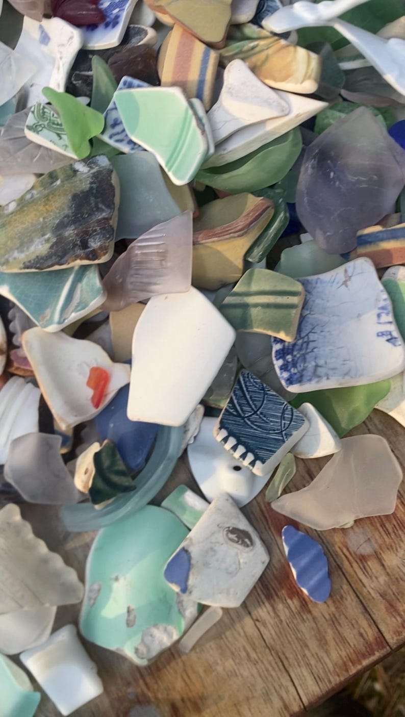 May include: A collection of sea glass and pottery shards in various colors, including white, blue, green, and yellow. The pieces have smooth, rounded edges and are of different shapes and sizes. The image shows a close-up view of the fragments.