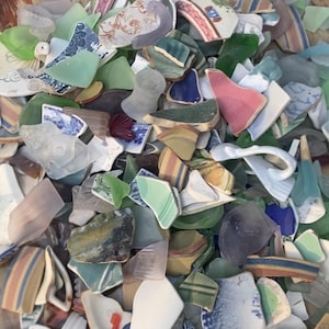 May include: A collection of sea glass and pottery shards in various colors, including green, blue, pink, and white. The fragments have different patterns and textures, creating a mosaic-like appearance. The pieces are of varying sizes and shapes.