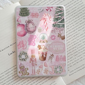 May include: Pink phone case with a festive Christmas design. Features illustrations of ornaments, candy canes, a nutcracker, and the text "Santa Baby" and "Sleighing My TBR".